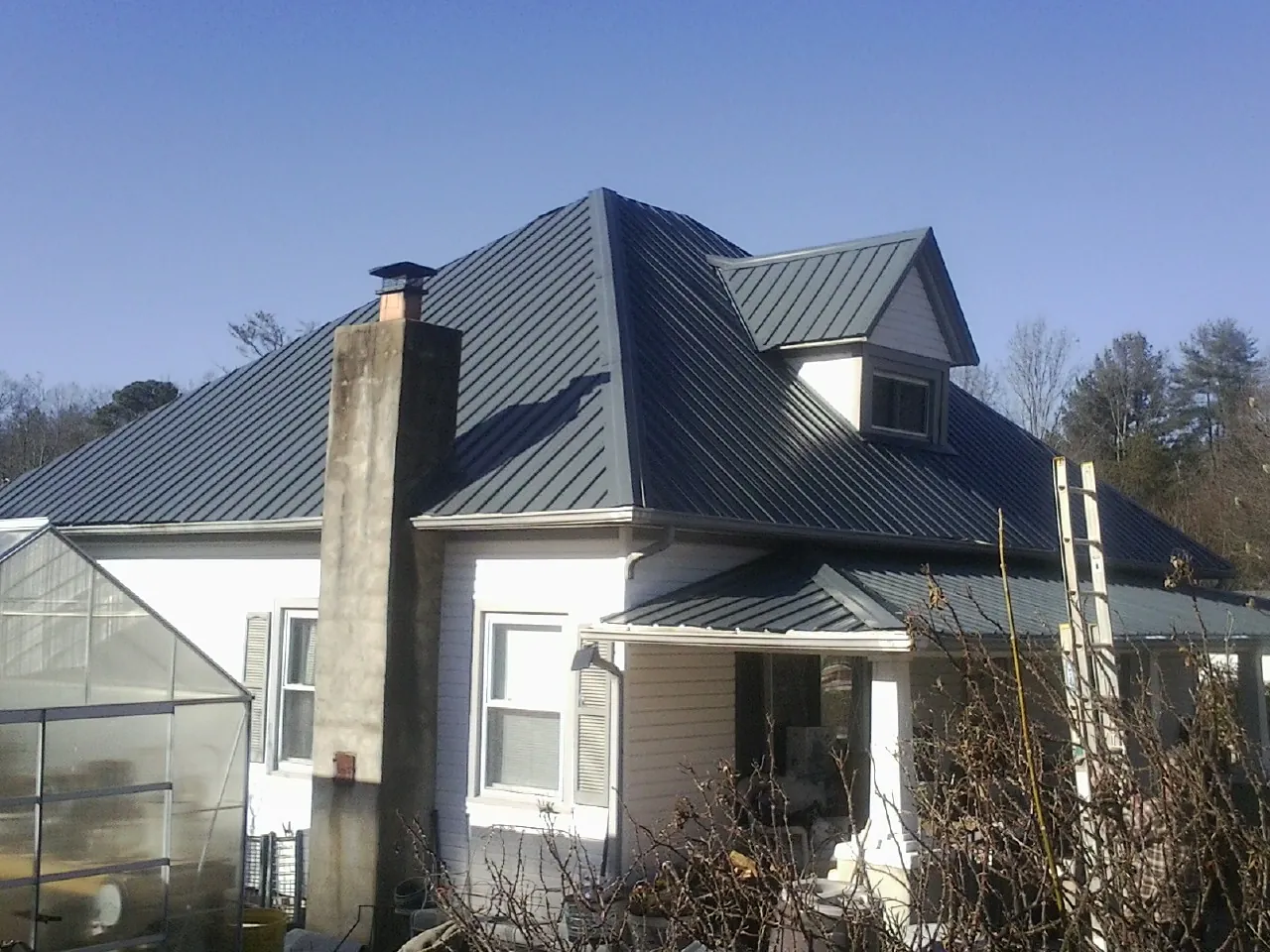 Dark blue standing seam metal roof on a white farmhouse with dormer — Slate & Tile Roof Repair by Roofing Brothers in Lady Lake