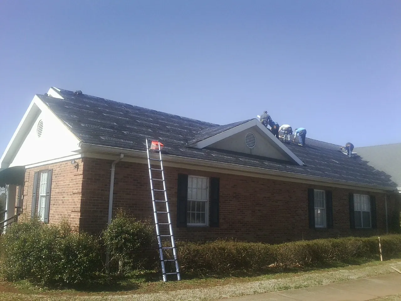 Crew tearing shingles off a brick ranch roof with a ladder set — Emergency Roof Repair work by our crew in Lady Lake