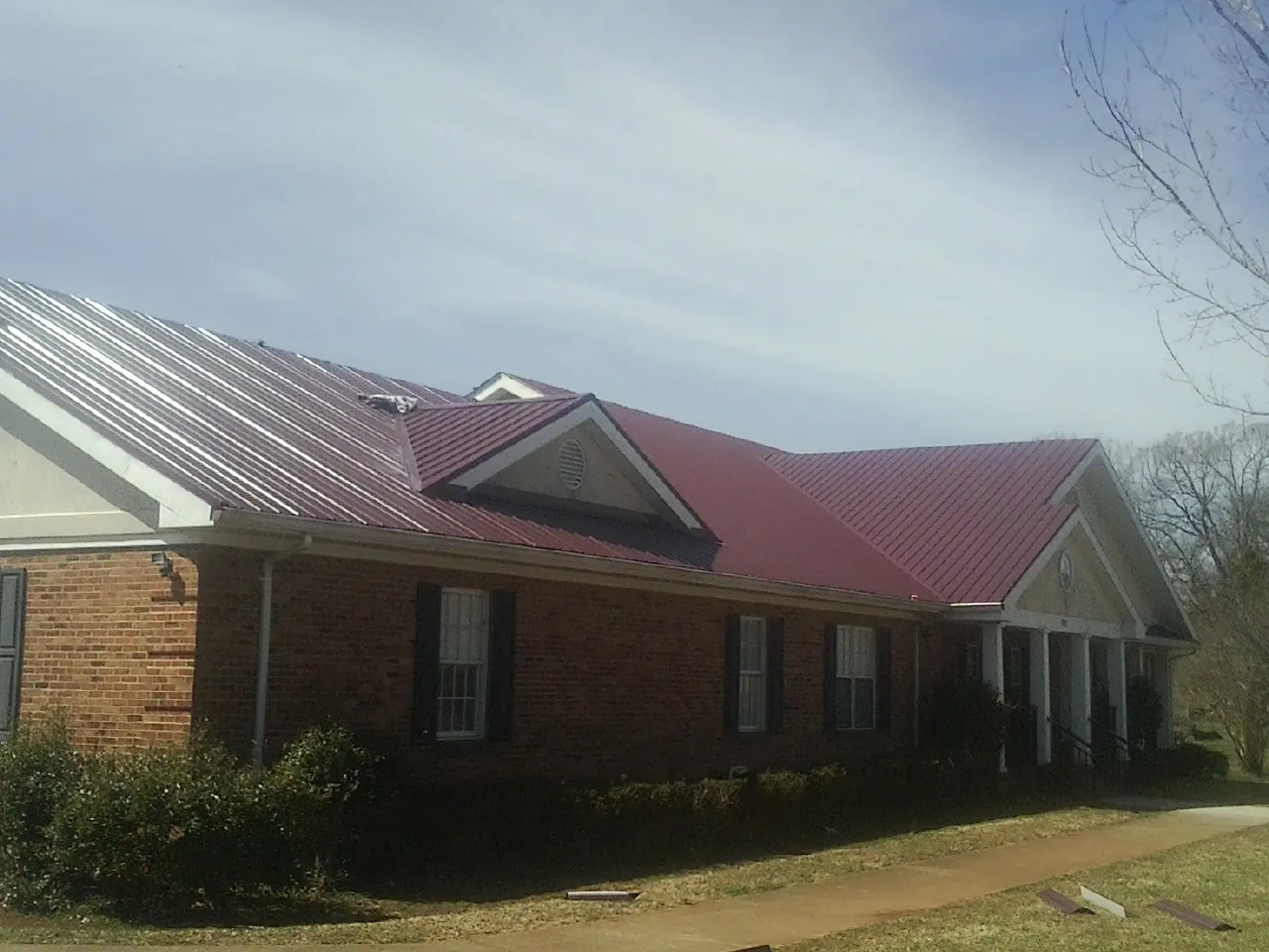 Red metal roof with gabled entries on a long brick building, from a Hail Damage Roof Repair job in Lady Lake
