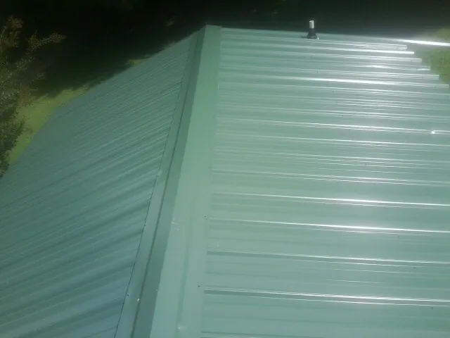 New green metal panels meeting at the ridge of a roof — Flat Roof Repair work by our crew in Lady Lake