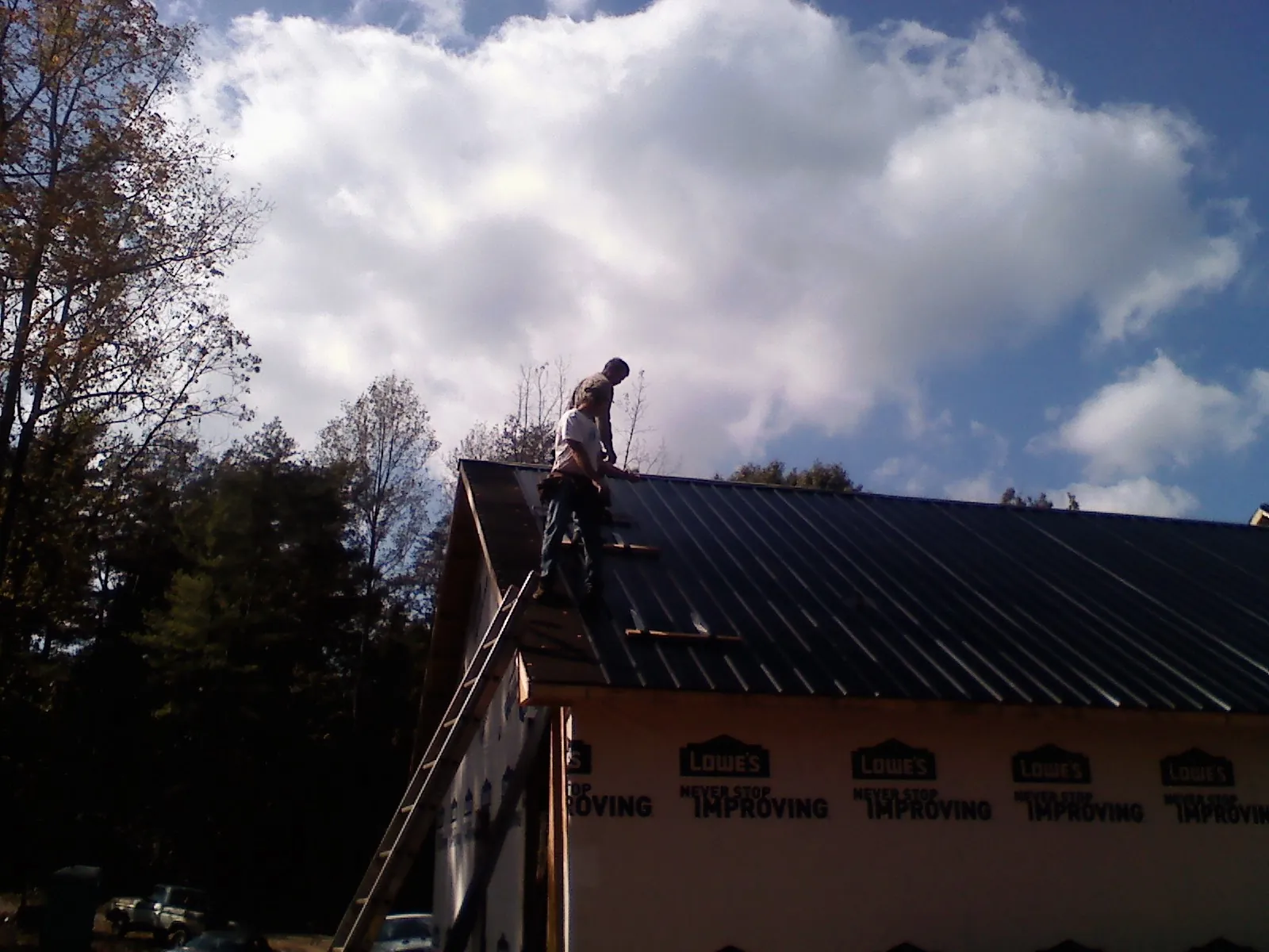 Roofer fastening dark metal panels high against a cloudy sky, from a Roof Inspection job in Lady Lake