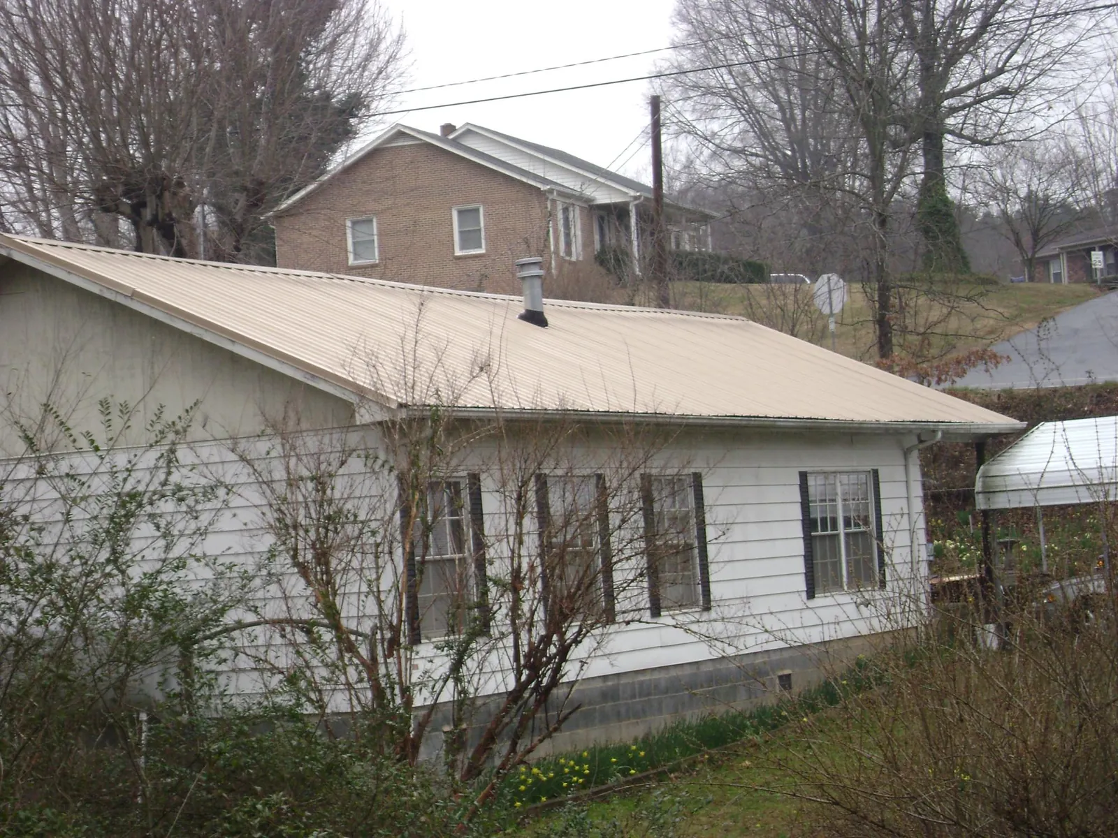 Tan metal roof on a white sided house set into a hillside — Commercial Roofing by Roofing Brothers in Lady Lake